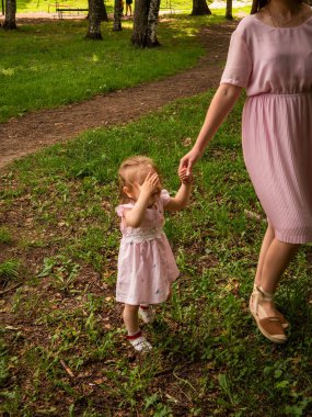 Anne ve kızı parkta yürüyüp oynuyorlar. Elbise giymişti. Güneşli bir gün, hafta sonu şehir parkında.