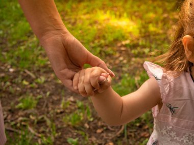 Anne ve kızı parkta yürüyüp oynuyorlar. Elbise giymişti. Güneşli bir gün, hafta sonu şehir parkında.
