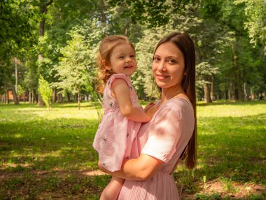 Anne ve kızı parkta yürüyüp oynuyorlar. Elbise giymişti. Güneşli bir gün, hafta sonu şehir parkında.