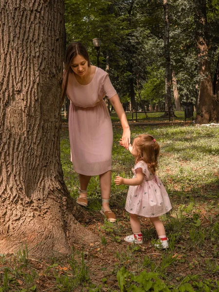 Mama i córka chodzą i bawią się w parku. Ubrana w sukienki. Słoneczny dzień, weekend w parku miejskim. — Zdjęcie stockowe