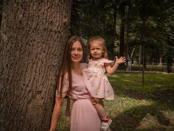 Mam en dochter lopen en spelen in het park. Gekleed in jurken. Zonnige dag, weekend in een stadspark. — Stockfoto