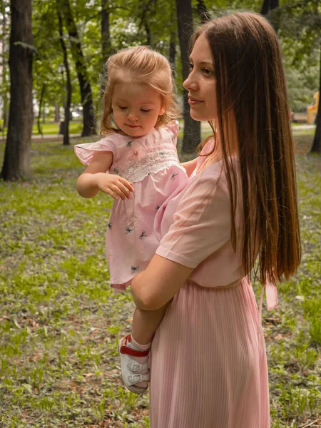 Mãe e filha caminham e brincam no parque. Vestido com vestidos. Dia ensolarado, fim de semana em um parque da cidade . — Fotografia de Stock