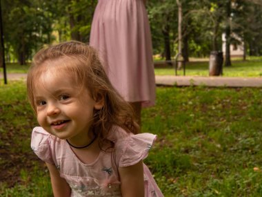 Anne ve kızı parkta yürüyüp oynuyorlar. Elbise giymişti. Güneşli bir gün, hafta sonu şehir parkında.