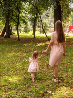 Anne ve kızı parkta yürüyüp oynuyorlar. Elbise giymişti. Güneşli bir gün, hafta sonu şehir parkında.