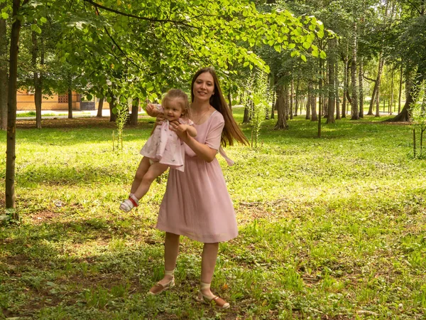 Mama i córka chodzą i bawią się w parku. Ubrana w sukienki. Słoneczny dzień, weekend w parku miejskim. — Zdjęcie stockowe