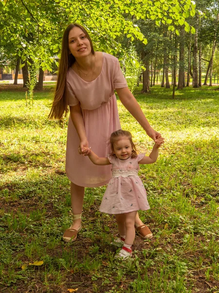 Mom and daughter walk and play in the park. Dressed in dresses. Sunny day, weekend in a city park. — Stock Photo, Image