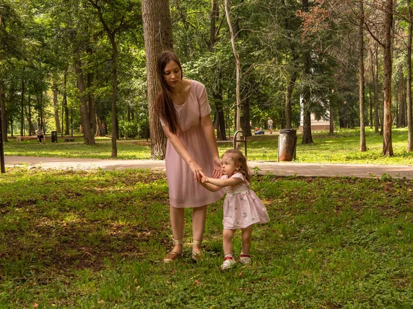 Mama i córka chodzą i bawią się w parku. Ubrana w sukienki. Słoneczny dzień, weekend w parku miejskim. — Zdjęcie stockowe