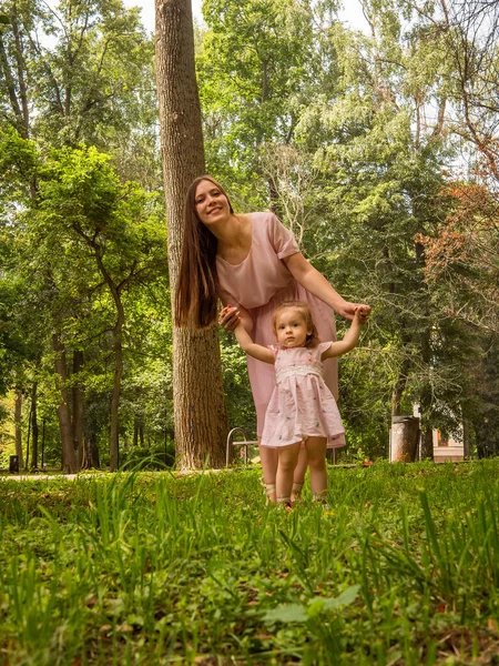 Mama i córka chodzą i bawią się w parku. Ubrana w sukienki. Słoneczny dzień, weekend w parku miejskim. — Zdjęcie stockowe