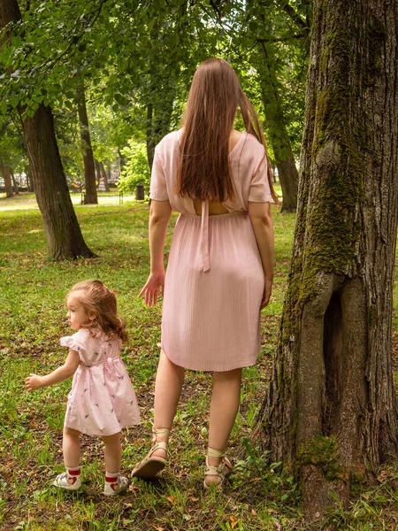 Mama i córka chodzą i bawią się w parku. Ubrana w sukienki. Słoneczny dzień, weekend w parku miejskim. — Zdjęcie stockowe