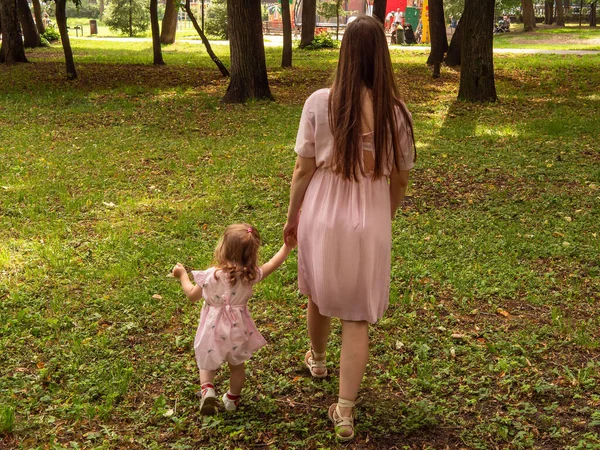 Mama i córka chodzą i bawią się w parku. Ubrana w sukienki. Słoneczny dzień, weekend w parku miejskim. — Zdjęcie stockowe