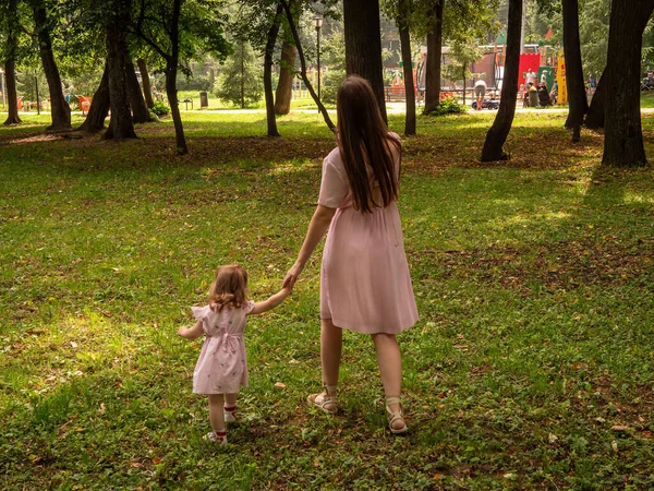 Mama i córka chodzą i bawią się w parku. Ubrana w sukienki. Słoneczny dzień, weekend w parku miejskim. — Zdjęcie stockowe