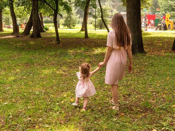 Mama i córka chodzą i bawią się w parku. Ubrana w sukienki. Słoneczny dzień, weekend w parku miejskim. — Zdjęcie stockowe