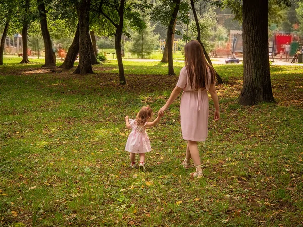 Mama i córka chodzą i bawią się w parku. Ubrana w sukienki. Słoneczny dzień, weekend w parku miejskim. — Zdjęcie stockowe