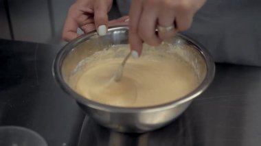 Hamuru çırpıcıyla yoğurmak. Dişi eller hamuru demir bir tabakta karıştırıyor..