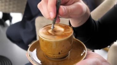 Bir adam elinde bir fincan kahve tutuyor, sandalyeye oturuyor. Gün