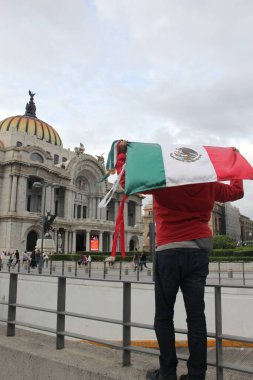 Mexico City, Mexico - 23 Ağustos 2023: Adam gururla CDMX şehir merkezindeki Palacio de Bellas Artes 'in önünde Meksika bayrağını kaldırdı.