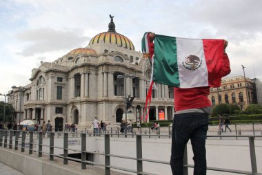 Mexico City, Mexico - 23 Ağustos 2023: Adam gururla CDMX şehir merkezindeki Palacio de Bellas Artes 'in önünde Meksika bayrağını kaldırdı.