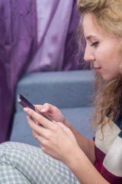 kanepede oturan telefon oynayan bir sıcak kazaklı kıvırcık saçlı kız