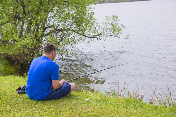 a man with a fishing rod fishing in the pond, on a Sunny lake sitting on the shore