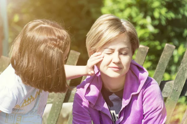 daughter and mom rest and hug in sunny weather, outdoors on a hot day