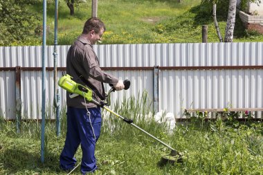 bir trimer gözlüklü bir adam köyde bir ev avlusunda çim mows, ülke topraklarının sipariş getiriyor