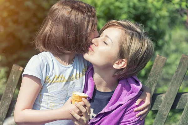 daughter and mom rest and hug in sunny weather, eat ice cream on a hot day