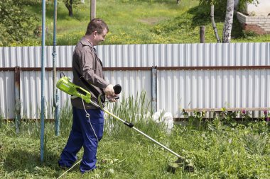 bir trimer gözlüklü bir adam köyde bir ev avlusunda çim mows, ülke topraklarının sipariş getiriyor
