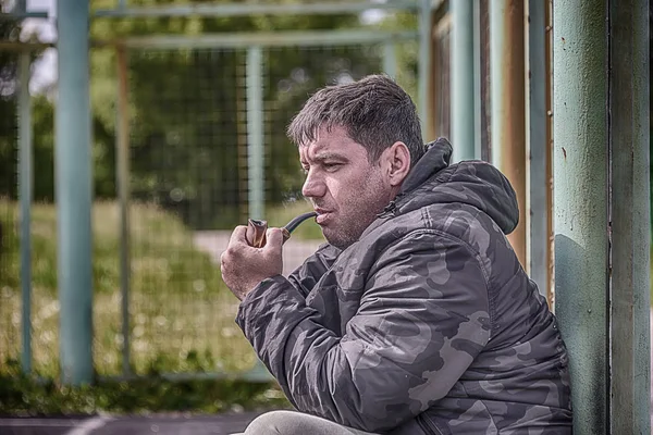 the man is smoking a pipe, close-up, in the cool windy weather, the smoke is flying in the air