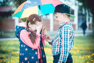 Çocuk bir şemsiye, bir oğlan ve bir kız dostça renkli bir şemsiye ile yaz aylarında yürüyüş ile parkta yürümek