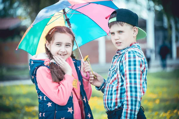 Çocuk bir şemsiye, bir oğlan ve bir kız dostça renkli bir şemsiye ile yaz aylarında yürüyüş ile parkta yürümek