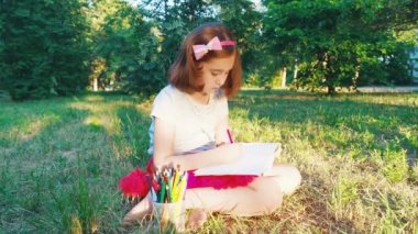 üstten görünüm bir orman parkta çimlere oturup albüm, kalem ile küçük sanatçı kız Kırmızı etekli çizer