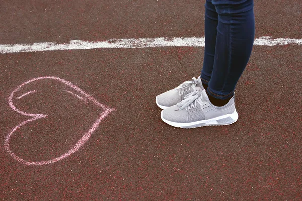 feet in shoes on asphalt, with a chalk-drawn heart