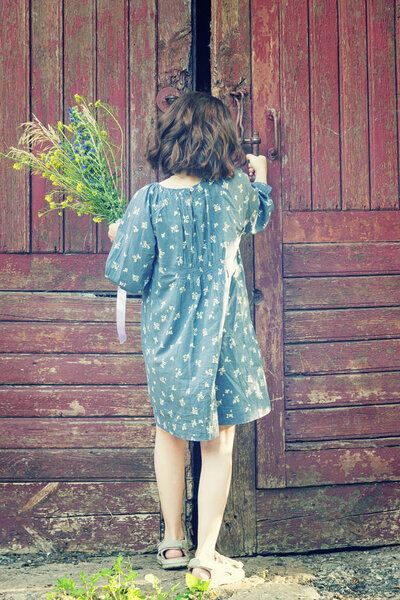 маленькая девочка смотрит в старую большую дверь разрушенного здания
