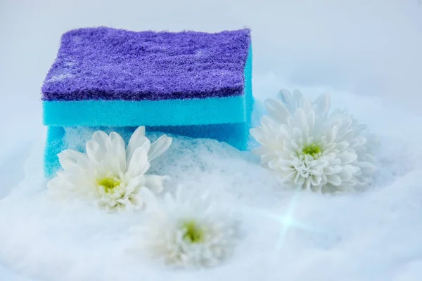 Sponge for washing dishes in soapy foam with flowers on white background