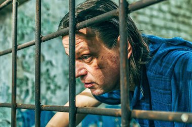 Parmaklıklar ardında elleri kelepçeli depresif bir adam. Depresyonda olan bir erkek suçlu hapse atıldı. Haykırıyor, kırıyor, ağlıyor.