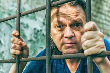 Parmaklıklar ardında elleri kelepçeli depresif bir adam. Depresyonda olan bir erkek suçlu hapse atıldı. Haykırıyor, kırıyor, ağlıyor.