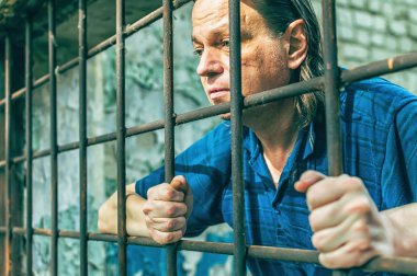 Parmaklıklar ardında elleri kelepçeli depresif bir adam. Depresyonda olan bir erkek suçlu hapse atıldı. Haykırıyor, kırıyor, ağlıyor.