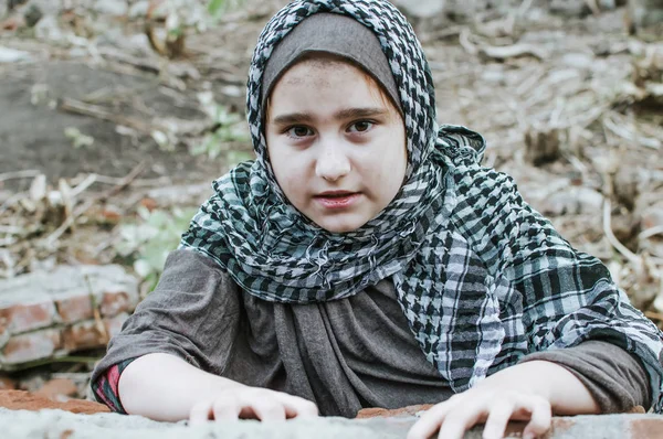 Un niño refugiado en la guerra, una niña musulmana con una cara sucia en las ruinas, el concepto de paz y guerra, el niño está llorando y esperando ayuda . — Foto de Stock