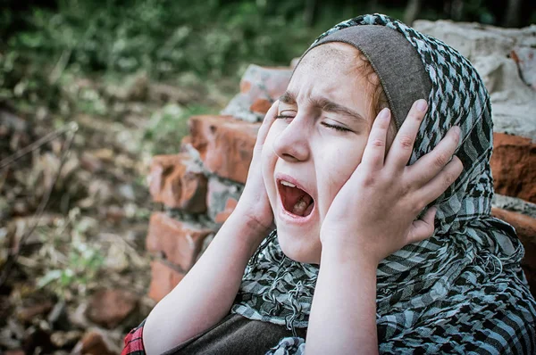 Un niño refugiado en la guerra, una niña musulmana con una cara sucia en las ruinas, el concepto de paz y guerra, el niño está llorando y esperando ayuda . — Foto de Stock