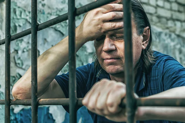 Un hombre deprimido esposado tras las rejas. Un delincuente detenido deprimido es encarcelado. Gritos, descansos, gritos . — Foto de Stock
