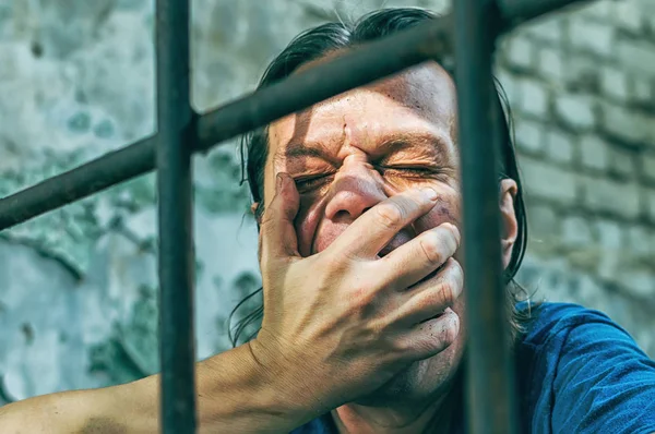 Un hombre deprimido esposado tras las rejas. Un delincuente detenido deprimido es encarcelado. Gritos, descansos, gritos . —  Fotos de Stock