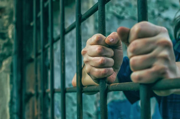 En deprimerad man i handbojor bakom galler. En deprimerad häktad man fängslas. Ropar, bryter, gråter. — Stockfoto
