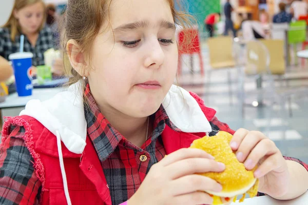 Hungry teenage girl eating a cheeseburger on the food court of the mall. Unhealthy food. — Stock Photo, Image