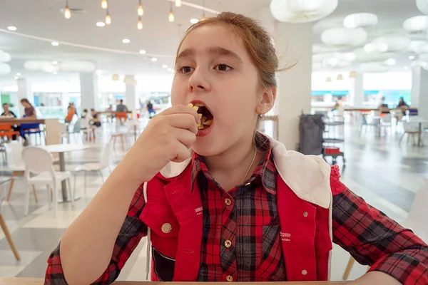 Hungry teenage girl eating french fries on the food court of the mall. Unhealthy food. — Stock Photo, Image