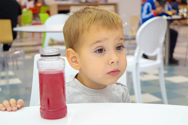Маленький ребенок пьет сок сидя за столом на фуд-корте торгового центра . — стоковое фото