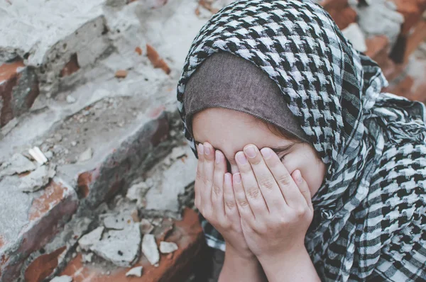 Un niño refugiado en la guerra, una niña musulmana con una cara sucia en las ruinas, el concepto de paz y guerra, el niño está llorando y esperando ayuda . — Foto de Stock