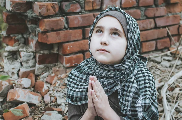 Ett flyktingbarn i kriget, en muslimsk flicka med ett smutsigt ansikte på ruinerna, begreppet fred och krig, barnet gråter och väntar på hjälp. — Stockfoto