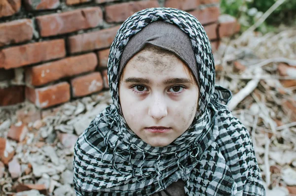 Un niño refugiado en la guerra, una niña musulmana con una cara sucia en las ruinas, el concepto de paz y guerra, el niño está llorando y esperando ayuda . — Foto de Stock