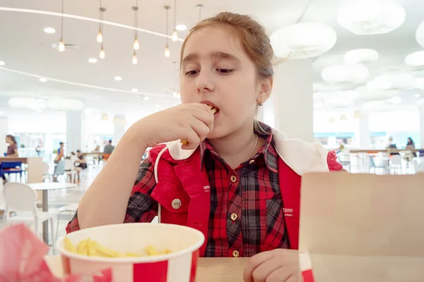 Hungry teenage girl eating french fries on the food court of the mall. Unhealthy food. — Stock Photo, Image