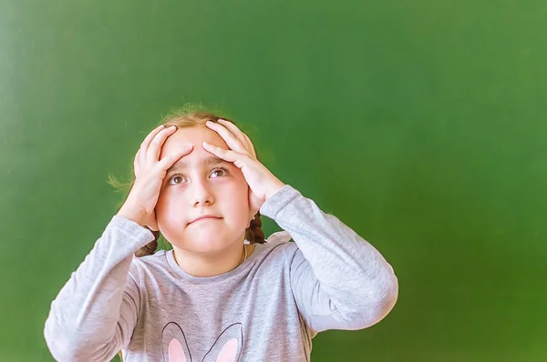 Retrato de una colegiala pensando en resolver un problema en la pizarra durante la lección . — Foto de Stock